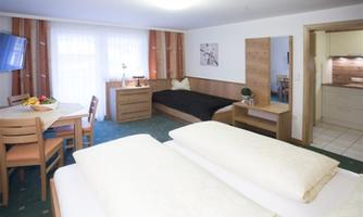 A cozy hotel room with two beds, a table and chairs. Large windows provide plenty of daylight.