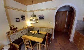 A cozy dining area with wooden chairs and a table. The walls are light, and there are decorative pictures as well as an entrance to another room.