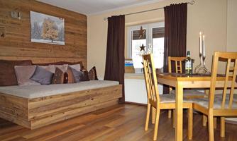 A cozy living space with a wooden bed and a dining table. The warm colors and the wood paneling create an inviting atmosphere.
