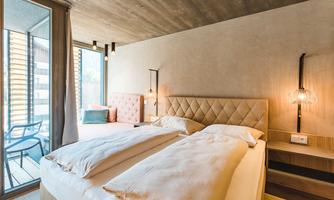 A modern hotel room with two beds and a large window. The room is bright and furnished in a minimalist style.