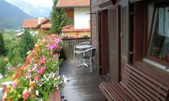 A beautiful balcony with blooming plants and a view of the mountains. A table and chairs invite you to relax.