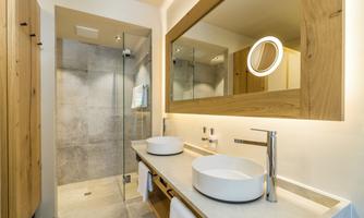 A modern bathroom with two sinks and a large mirror. The shower is transparent and the furniture is made of wood.