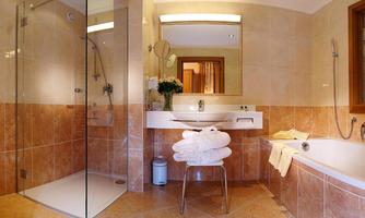 A modern bathroom with a glass shower enclosure and a bathtub. The decor is elegant and clean, adorned with towels and fresh flowers.