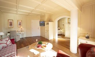 A bright living room with elegant furniture and warm wooden floors. White walls and large windows create an inviting atmosphere.