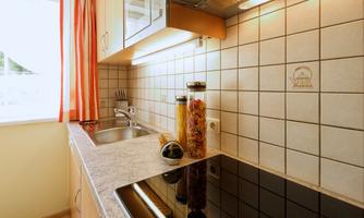 A modern kitchen with a smooth cooktop and a sink. On the countertop, jars filled with pasta and spices are decoratively placed.