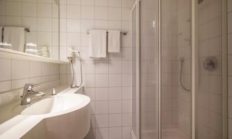 A modern bathroom with a shower and a sink. The walls are tiled with white tiles and there are fresh towels.