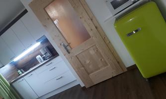 A modern kitchen with a green refrigerator and wood accents. The space has a warm atmosphere with plenty of light.