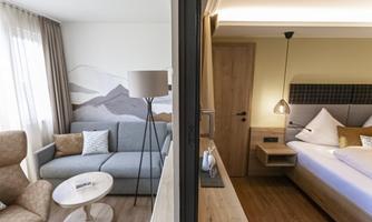 A stylish hotel room combination featuring a cozy living area and an elegant bedroom. The modern furnishings and natural colors create an inviting atmosphere.