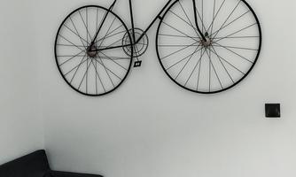A black bicycle is hung on the wall. In the room, there is a gray sofa.