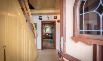 An inviting entrance area with a wooden staircase and a large door window. The room is bright and cozy, with a view of the living room in the background.