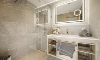 A modern bathroom with a walk-in shower and large mirrors. The walls are clad with light tiles, and a stylish wooden chest of drawers stands in the room.