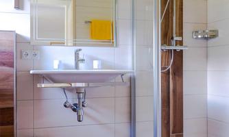 A modern bathroom with a shower and a large mirror surface. The floor is made of wood and there is a towel holder with a yellow towel.