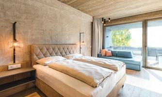 A modern bedroom with a large double bed and soft colors. There is a cozy seating area on the balcony.
