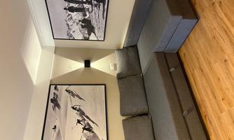 A modern living room with a gray couch and two large black-and-white pictures on the wall. The floor is made of wood, creating a cozy atmosphere.