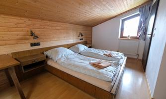 A cozy bedroom with two single beds and wooden paneling. The room has a window with daylight and a modern decor.