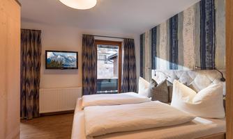 A cozy bedroom with two single beds and modern pillows. A television and a window with a view outside complete the room.