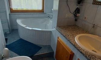 A modern bathroom with a bathtub, a sink, and a window with a view. The floor is covered with gray tiles and there are wooden cabinets.