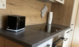 A modern kitchen with wooden walls and a clear work surface. On the counter are a kettle and a vase.