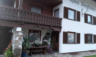 A cozy house named "Haus Bergfrieden." The entrance area is beautifully decorated with flowers and plants.