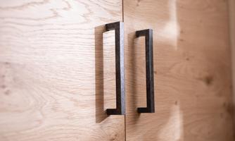 A wooden cabinet with two modern, black handles. The surface is made of light wood with a natural grain.