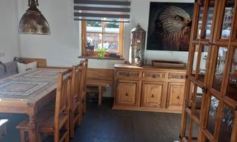 A cozy dining area with a wooden table and chairs. A large picture of a bird hangs on the wall, and there is a wooden display cabinet.