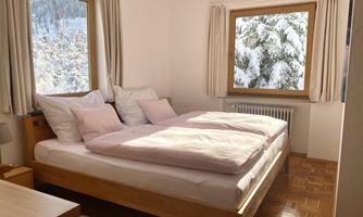 A bright bedroom with a large double bed and cozy pillows. A snowy landscape can be seen through the window.