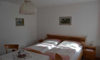 A cozy bedroom with a double bed and bright bedding. Two pictures hang on the wall and a table is decorated with a tablecloth.