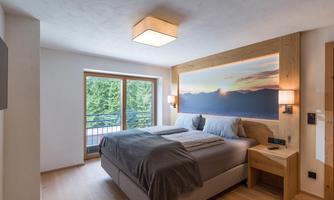 A modern bedroom with a large double bed and cozy blankets. The windows offer a view of a green landscape.