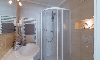 A modern bathroom with a shower and a sink. The walls are painted in light colors and there are towels in neutral tones.