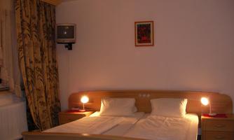 A simple bedroom with a double bed and two nightstands. A picture is hanging on the wall, and there is a television in the corner.