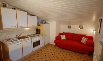 A cozy attic apartment with a red couch and a small kitchenette. The room has a bright and friendly atmosphere.