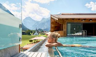 A relaxed person in the pool with a view of the mountains. The sky is clear and the surroundings are calm and idyllic.