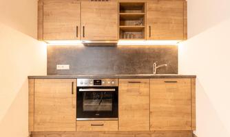 A modern kitchen with wooden furniture and an elegant countertop. It features a stove, an oven, and a stone wall covering.
