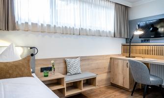A modern room with a single bed, a desk, and a chair. Bright curtains let in plenty of light and create a pleasant atmosphere.