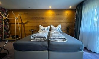 A modern bedroom with two single beds and elegant bedding. The walls are made of wood, and there are large windows with curtains.