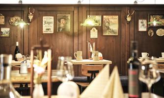 A cozy restaurant with wooden walls and rustic decor. There are tablecloths, wine glasses, and many pictures on the walls.