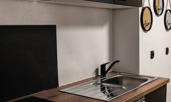 A modern kitchen with black cabinets and a wooden countertop. The room contains a sink, a stovetop, and a small freezer.