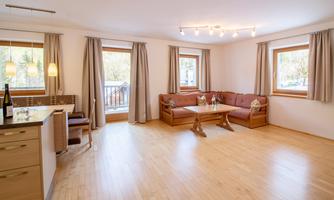 A modern living room with light walls and wooden floors. There are comfortable sofas, large windows, and a cozy atmosphere.