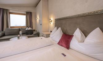 A stylish hotel room with two beds and a cozy sofa. Large windows provide a view outside and bring plenty of daylight into the room.