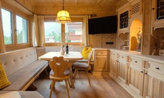 A cozy dining area made of wood with a large table and a bench-like seating arrangement. The room is brightly lit and offers a view outside.