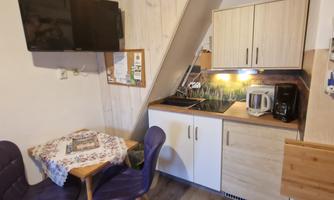 A cozy kitchen with a small dining table and two chairs. A TV hangs on the wall and the kitchen is modernly decorated.