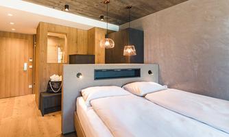 A modern furnished bedroom with wooden paneling and comfortable beds. The warm lighting accents create a cozy atmosphere.