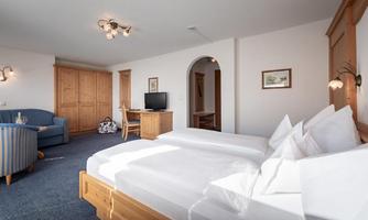 A bright room with two single beds, a television, and a cozy sitting area. The furniture is made of wood and conveys a warm atmosphere.