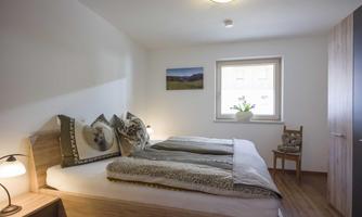 A cozy bedroom with two beds and modern furniture. Bright walls and a window create an inviting atmosphere.