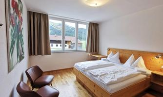 A cozy hotel room with wooden furniture and a large window.  
In the room, there are two beds and two chairs, and there is a painting on the wall.