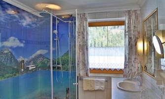 A modern bathroom with a shower cabin and a sink. The wall is decorated with a beautiful landscape motif of mountains and a lake.