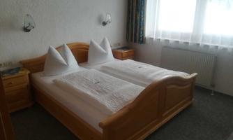 A cozy bedroom with a double bed and two nightstands. The walls are light and large windows let in plenty of daylight.