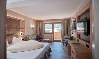 A modern bedroom with wooden furniture and a large window. The room is bright and inviting, with a cozy bed and a television.