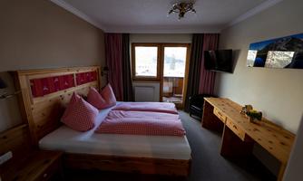 A cozy hotel room with two beds and red-and-white checked pillows. There is a window with a view outside and a flat-screen TV on the wall.