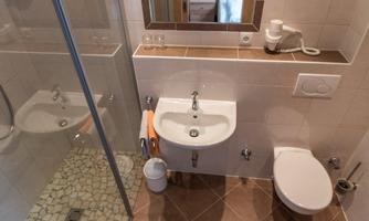 A modern bathroom with a shower, sink, and toilet. The floor is tiled and there is a mirror above the sink.